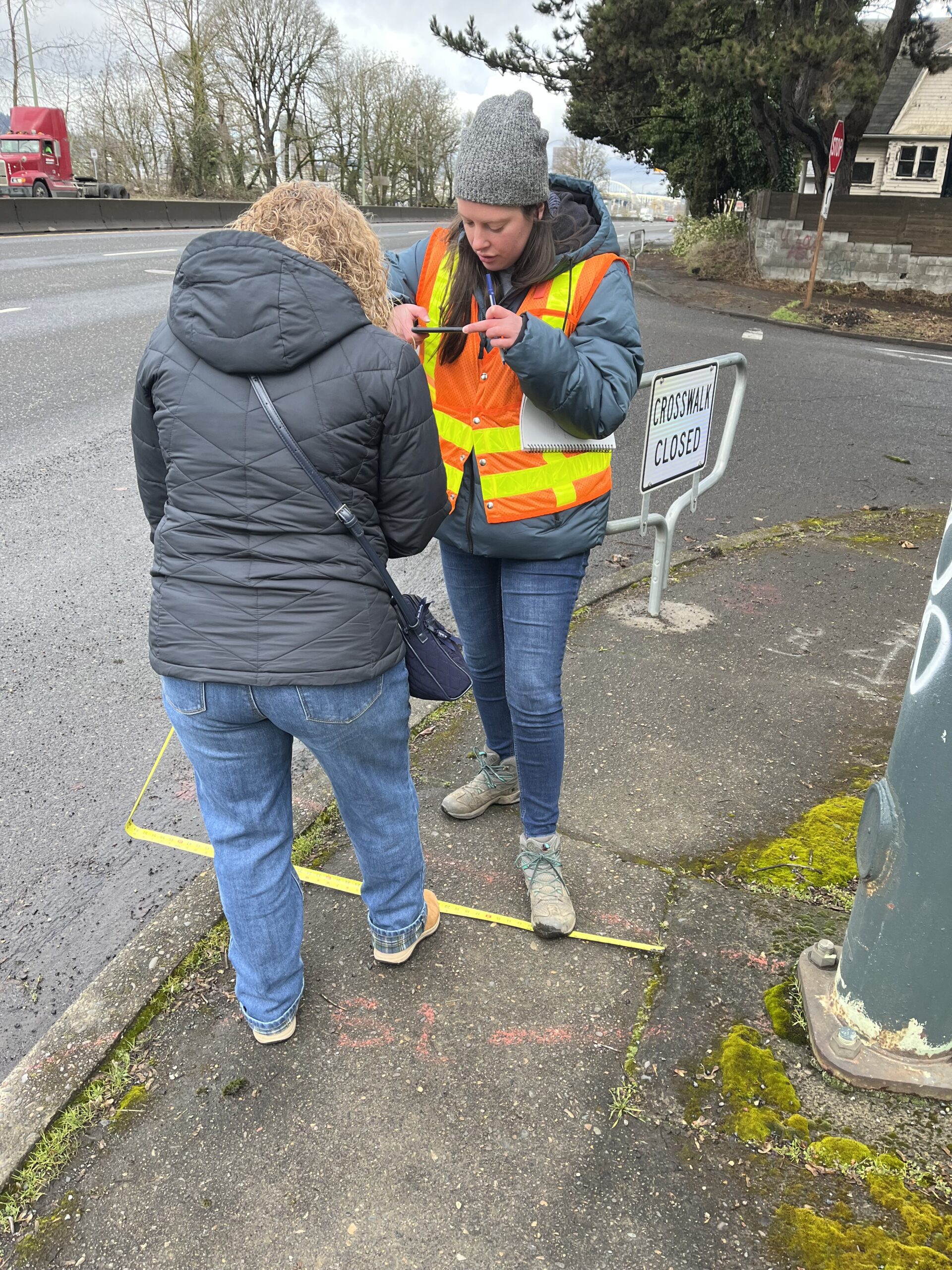 Two individuals take accessibility measurements on a sidewalk